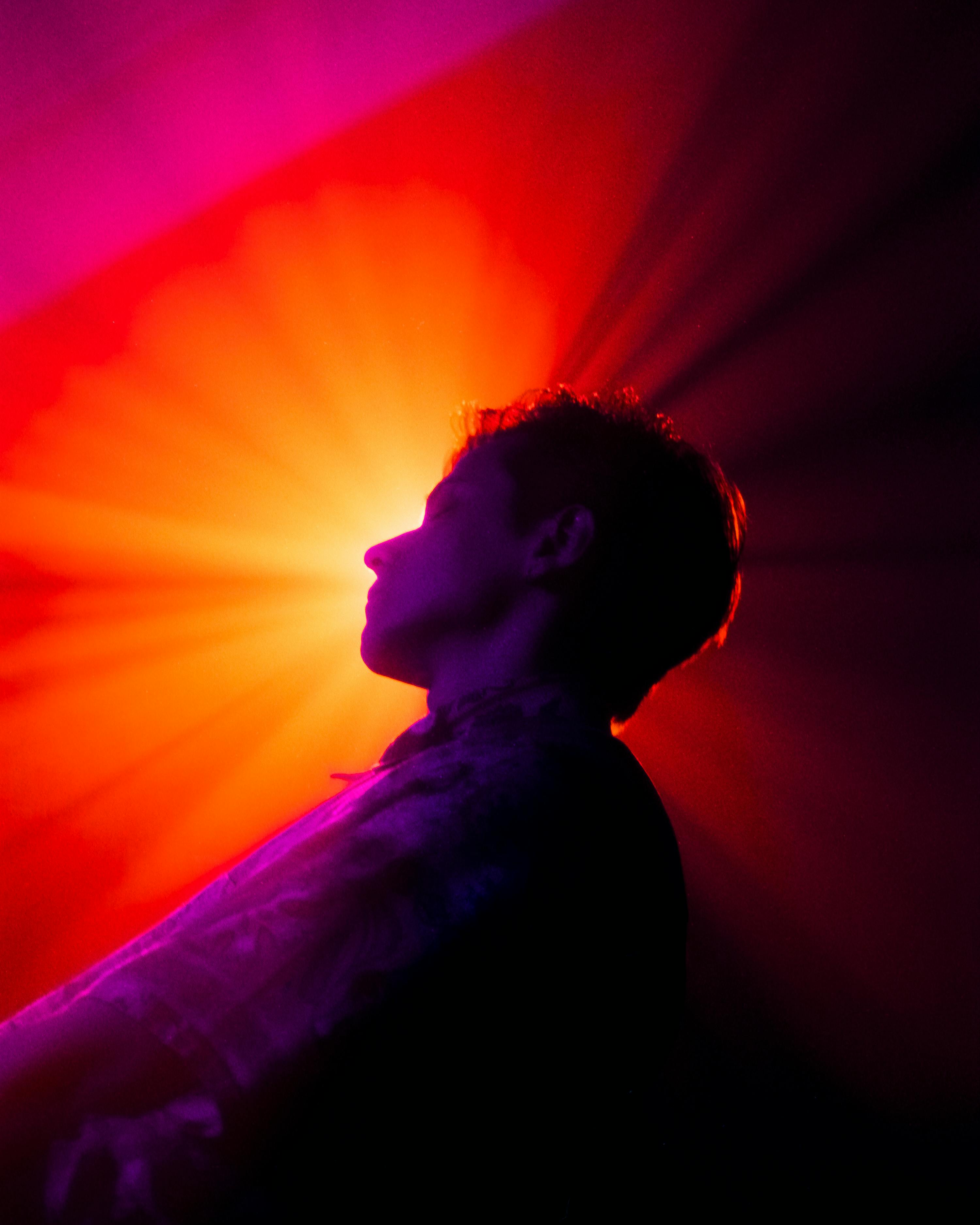 A dramatic silhouette of a person against a vibrant orange and purple background lighting.