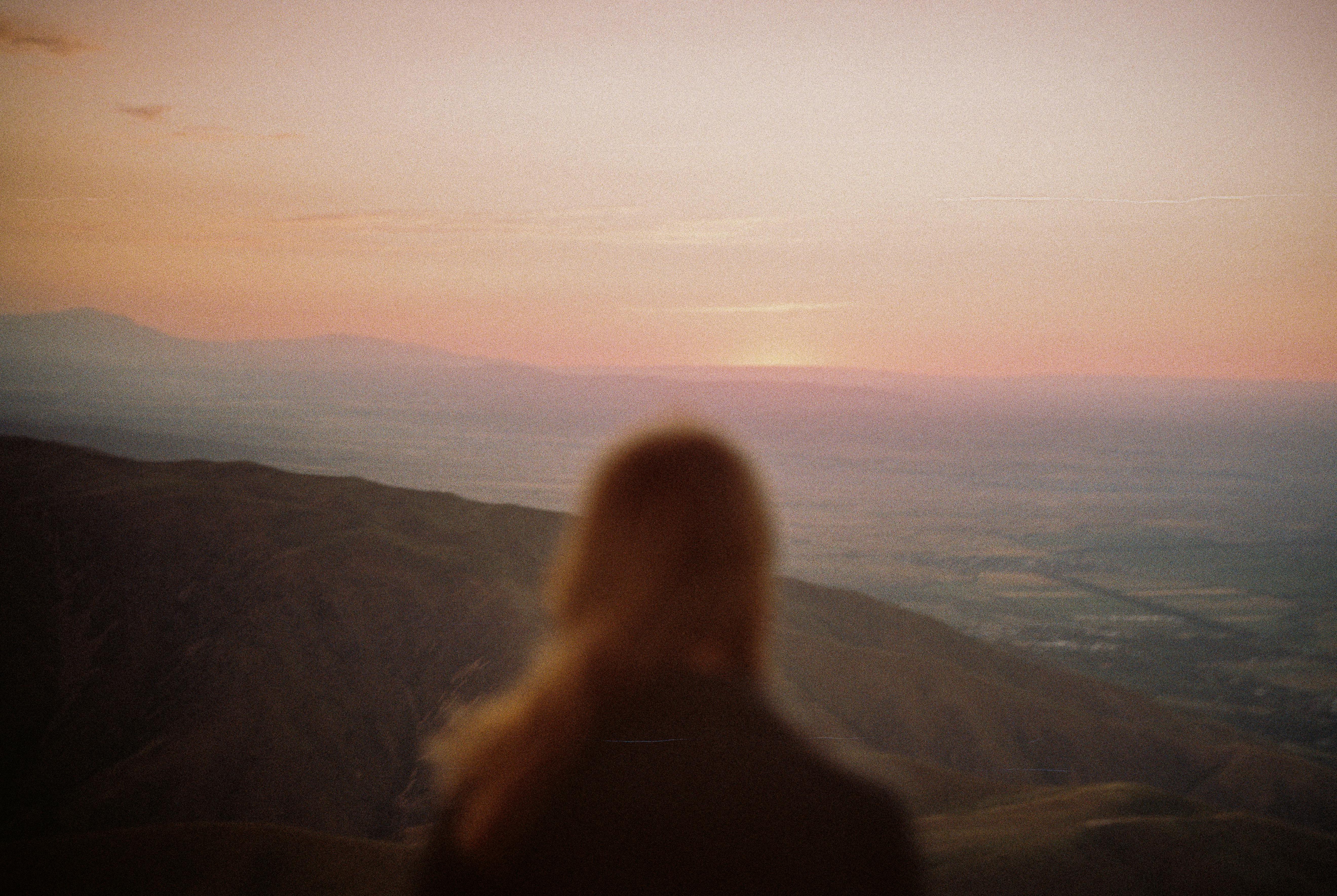 Silhouette of a woman overlooking Almaty mountains at sunset, creating a serene landscape.