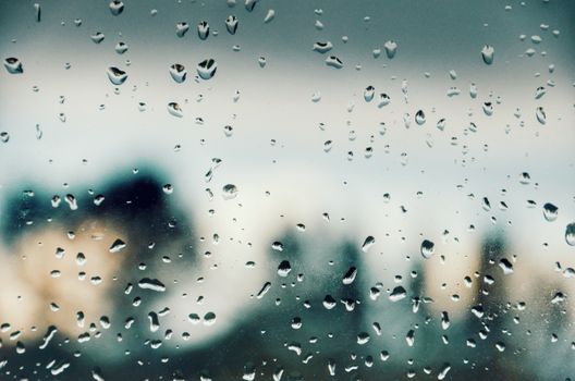 Raindrops on a window pane with a blurry city skyline in the background.