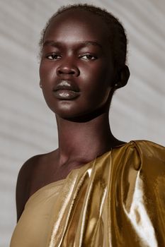 Striking studio portrait of a young woman in gold fabric, captured in natural light.