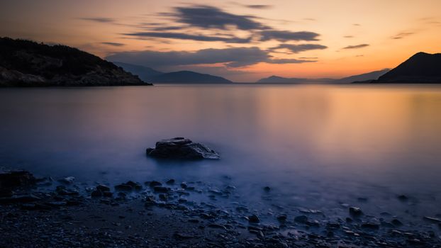 Serene sunset view over calm waters and rocky shore in Erateini, Greece, perfect for nature lovers.