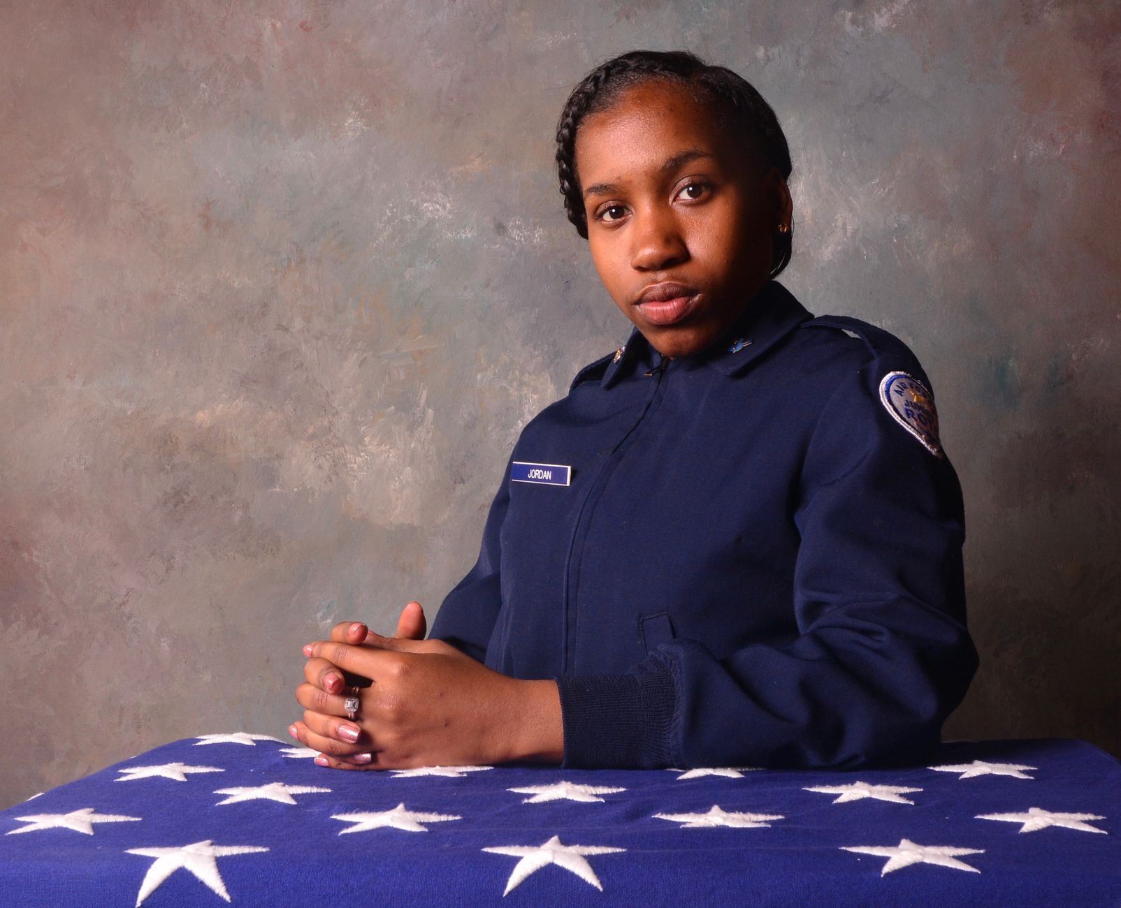 Portrait of a young woman in uniform with hands together on a star-spangled cloth.