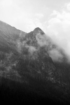 Black and white photo of a foggy mountain peak creating a dramatic atmosphere.