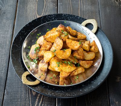 Close-up of crispy seasoned potato wedges garnished with herbs, elegantly served on a decorative plate.