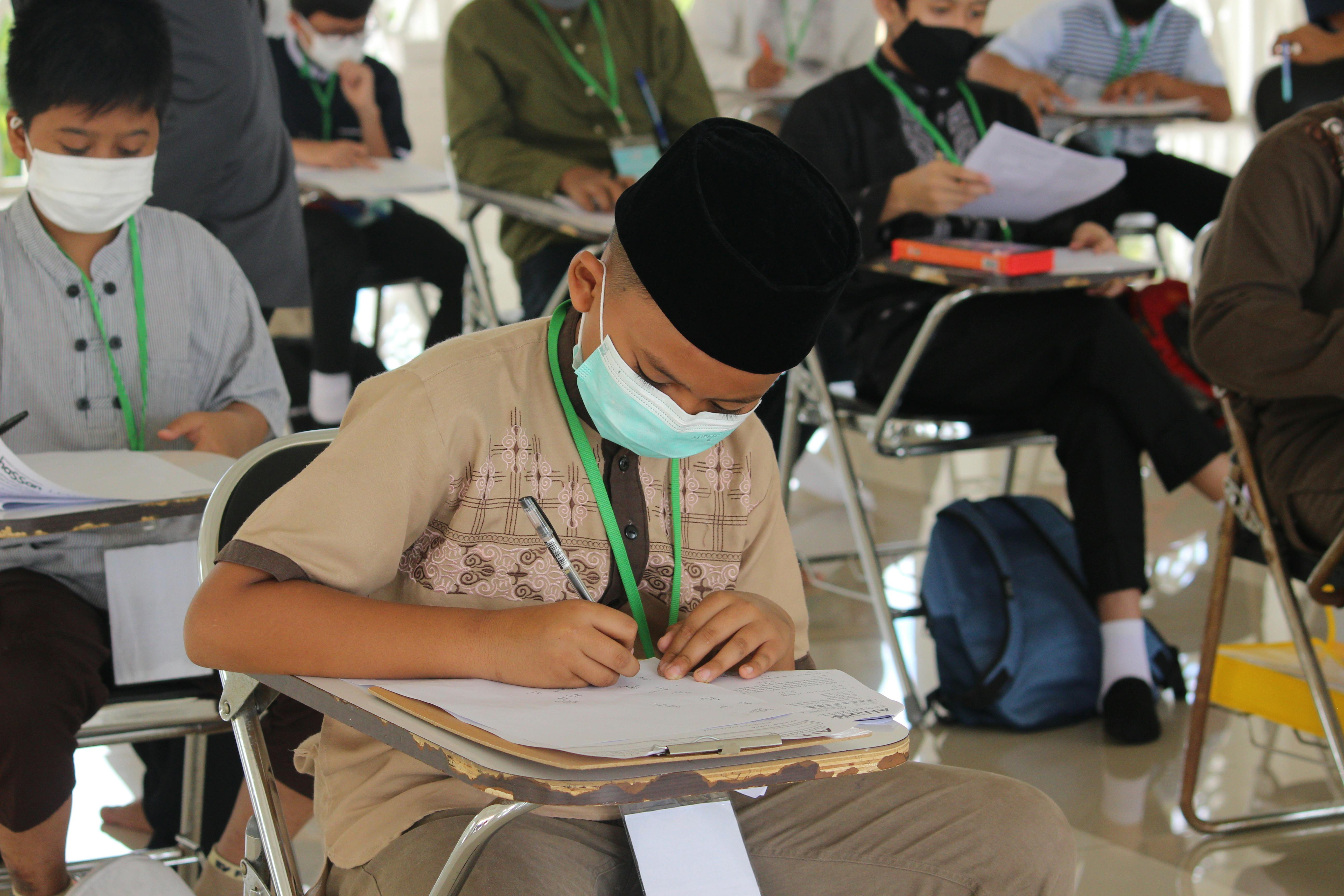 Children wearing face masks studying in a classroom, practicing social distancing for safety.