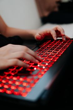 Hands typing on a red backlit keyboard, close-up view, emphasizing technology and digital interaction.