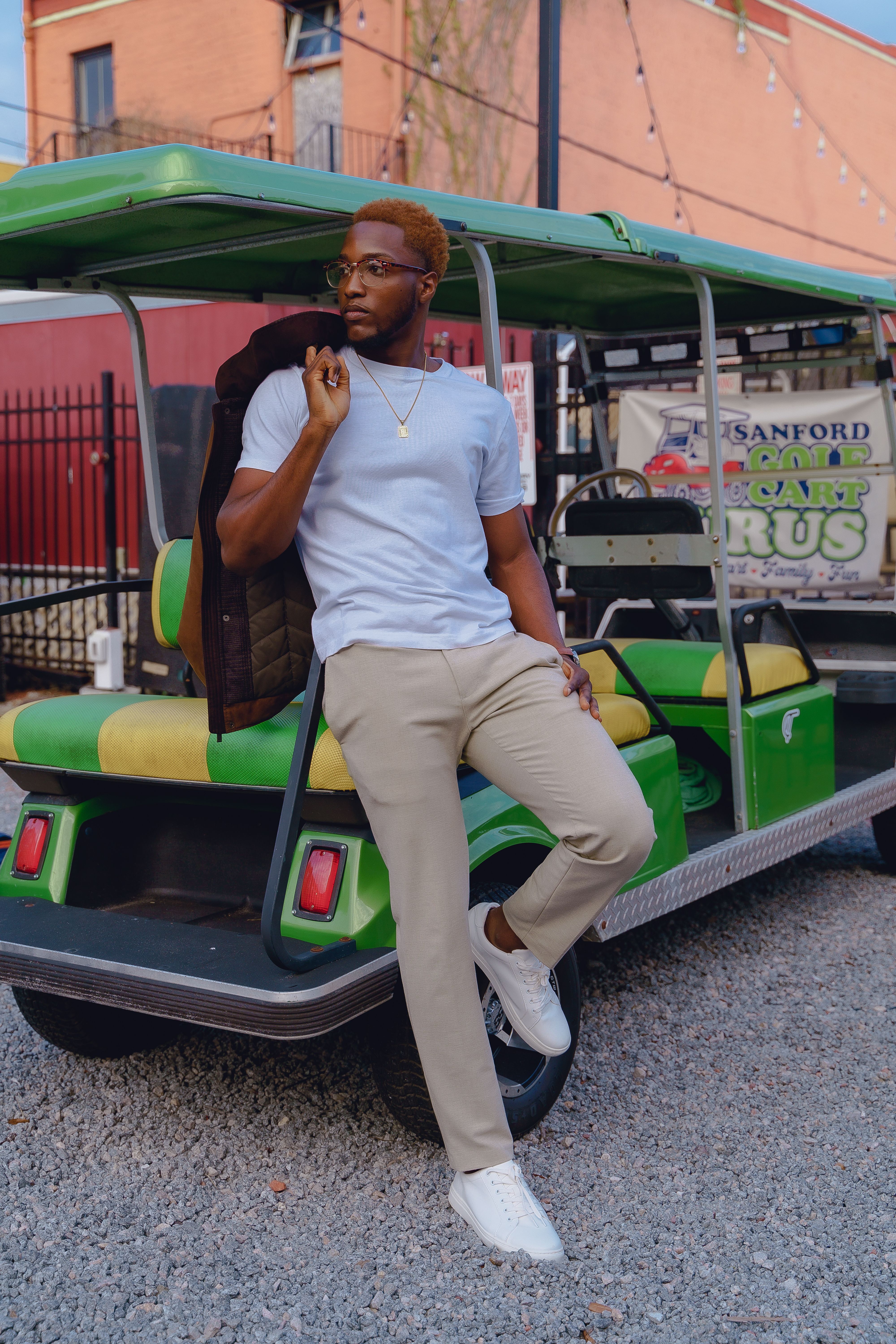 A fashionable man stands by a green golf cart in Sanford, Florida, showcasing modern style and confidence.