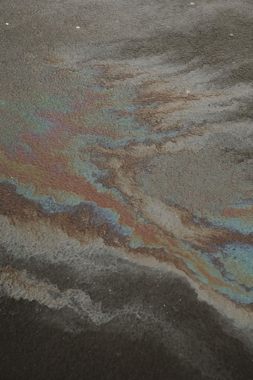 Free Detailed view of iridescent oil spill patterns on a textured pavement surface. Stock Photo