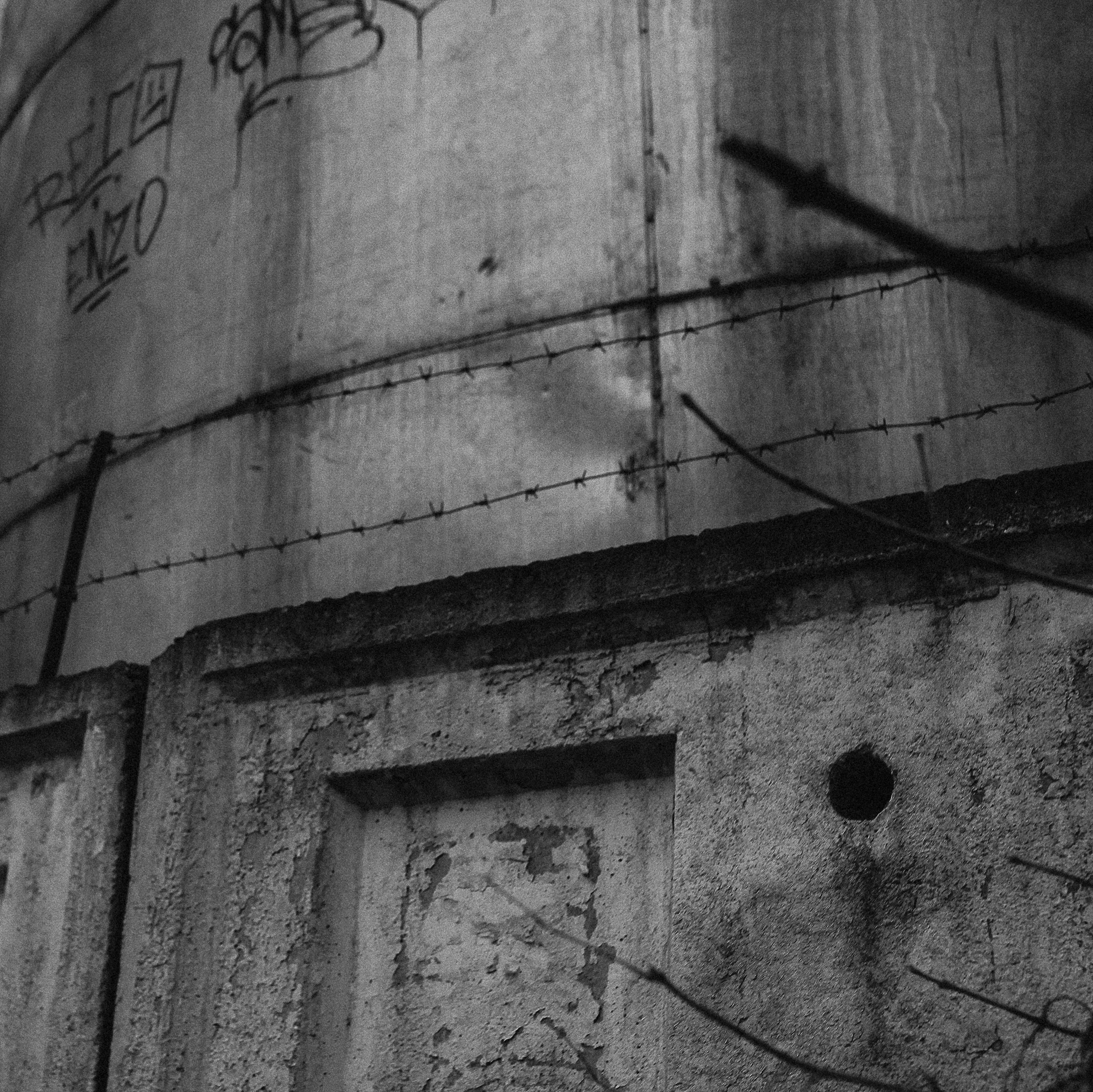Grayscale image of a rough concrete wall with barbed wire, showcasing urban decay.