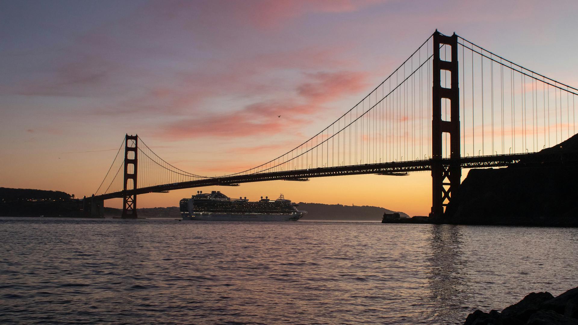 A breathtaking view of the Golden Gate Bridge and a cruise ship during a colorful sunset in San Francisco.