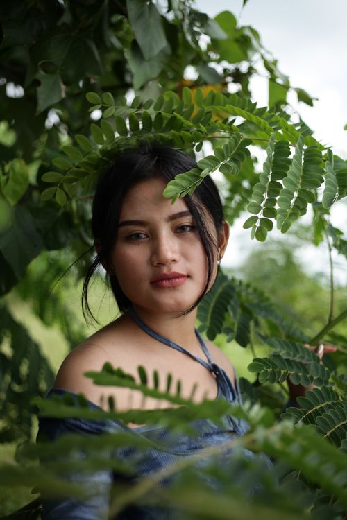 Free Beautiful portrait of an adult woman surrounded by lush green leaves in an outdoor setting. Stock Photo