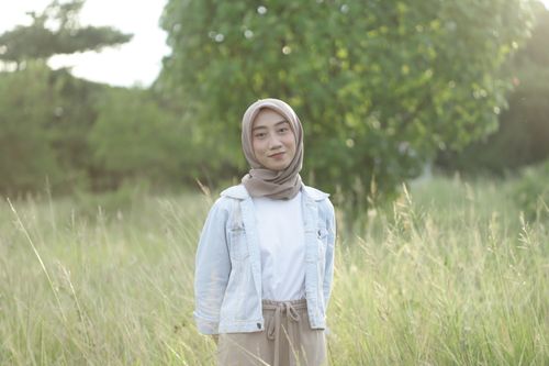 Free A cheerful woman in a hijab smiles in a sunlit field, wearing casual attire. Stock Photo