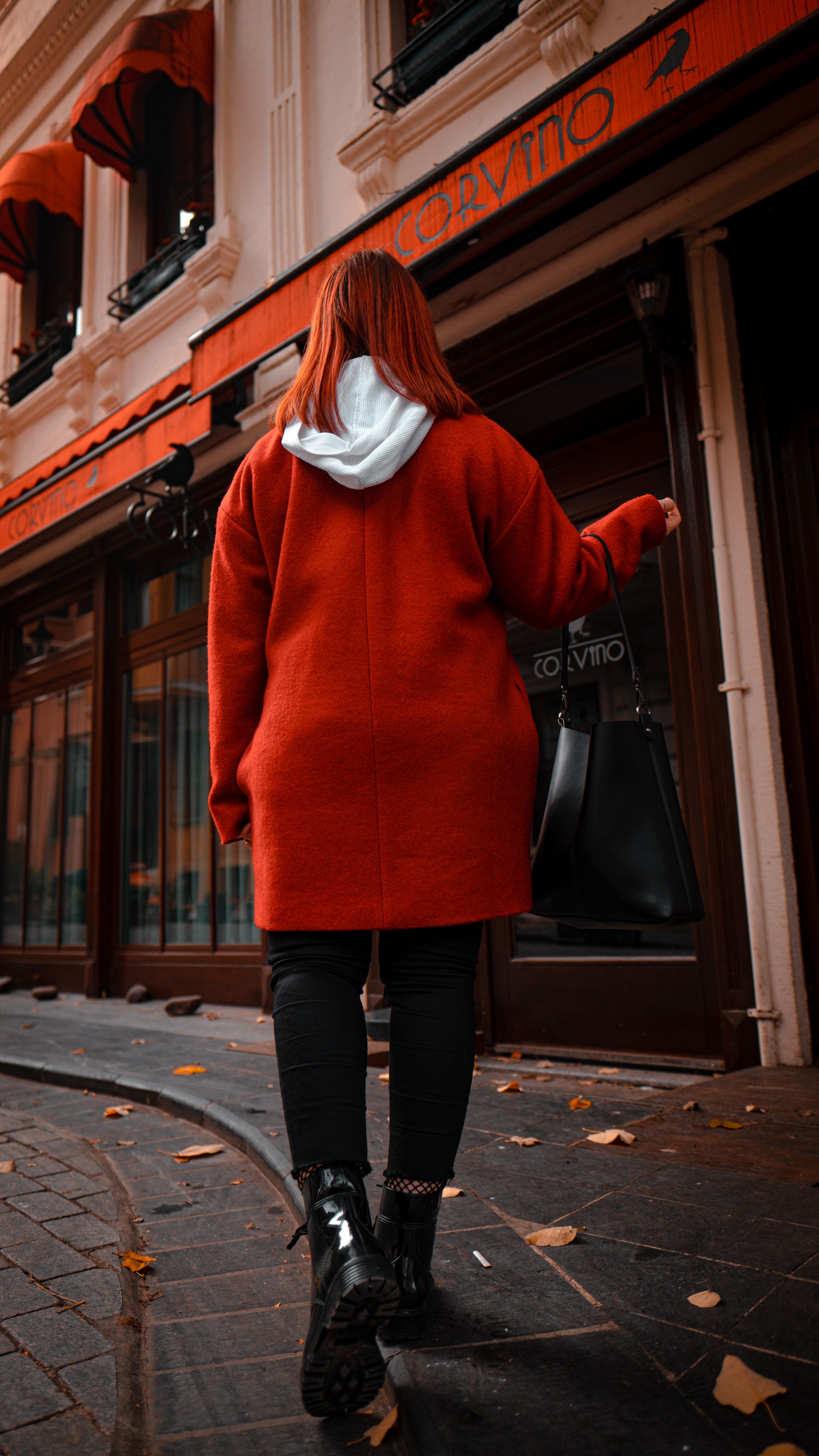 Back view of a redhead woman in a red sweater walking down a city street.