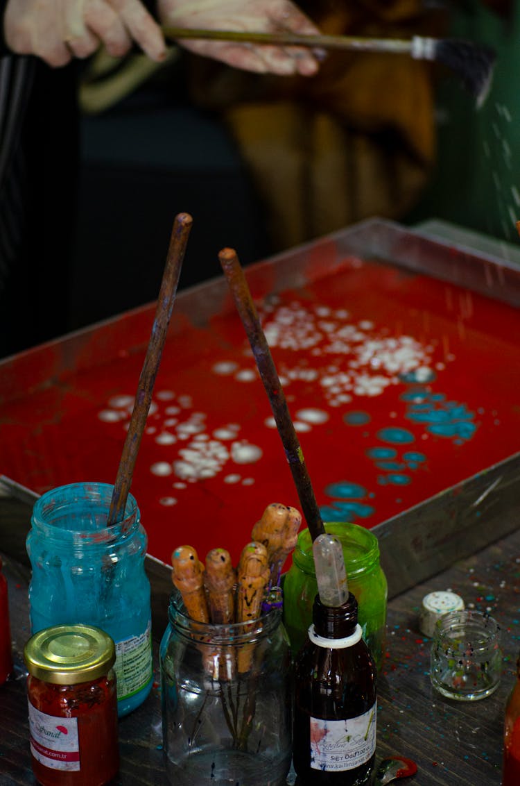 Person Doing Paint Droplets On Metal Tray Beside Art Materials On The Table
