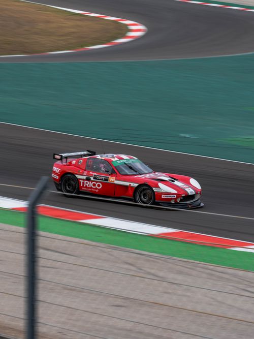 Free Red race car speeding down a winding race track during a motorsport event. Stock Photo