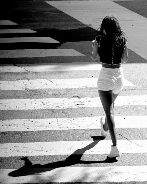 Grayscale Photo of a Woman Walking on the Pedestrian Lane