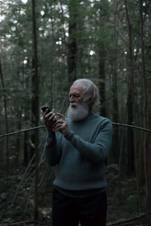 Free Senior man with grey hair and beard using smartphone in a forest setting. Stock Photo