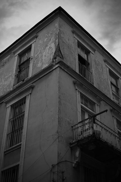 Free Atmospheric black and white photo of a decaying building corner with barred windows. Stock Photo