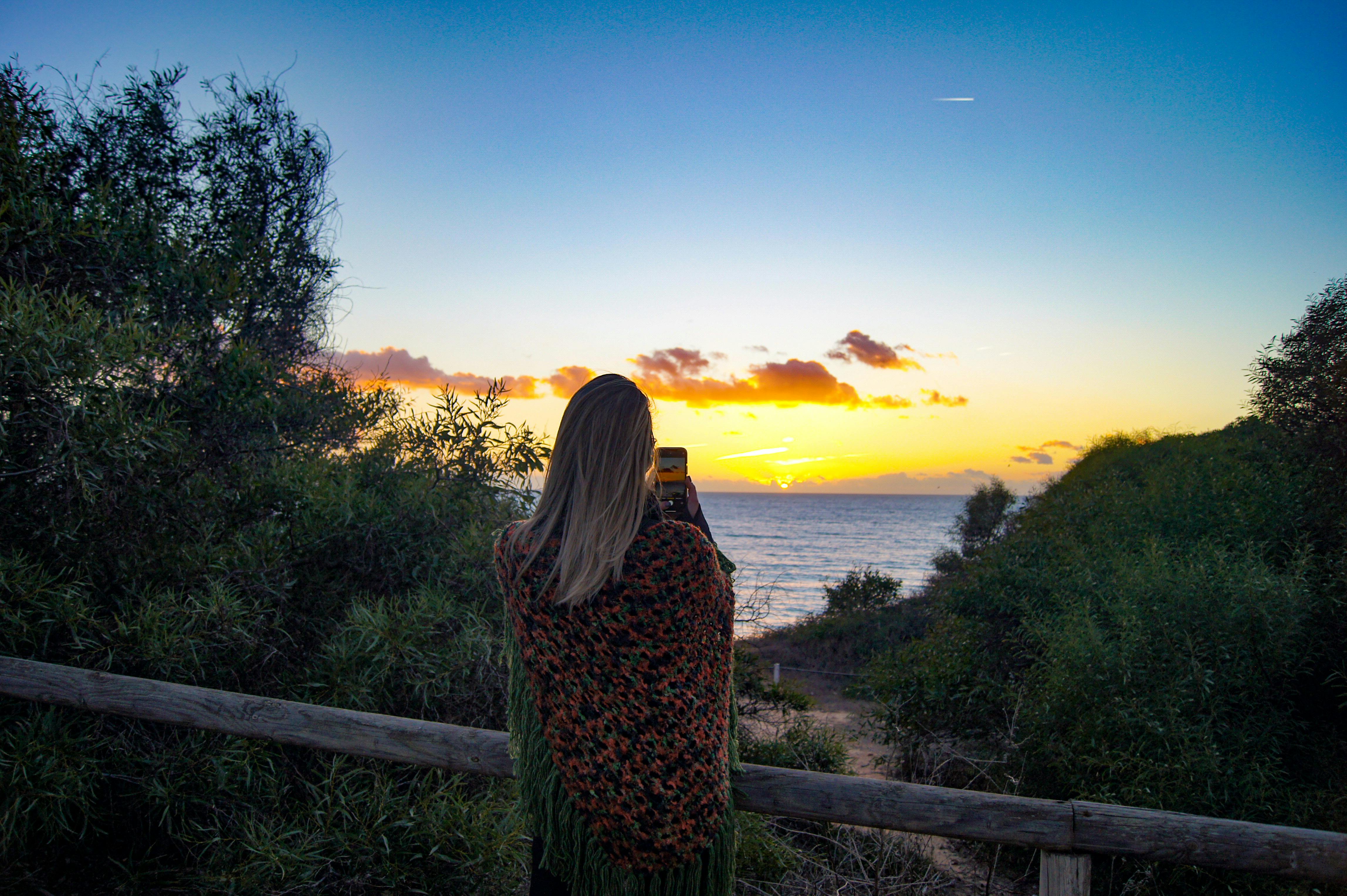 Femme photographiant un coucher de soleil sur l'océan au Portugal