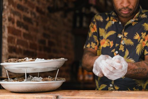 Free A man prepares oysters on ice with precision in a rustic setting, showcasing culinary skill. Stock Photo