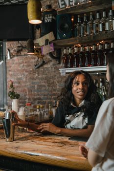 Bartender chatting with a customer at a rustic bar with bottle display.