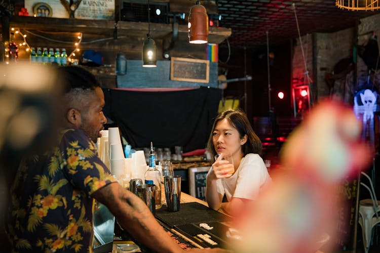 Female Customer And Bartender Talking At Bar