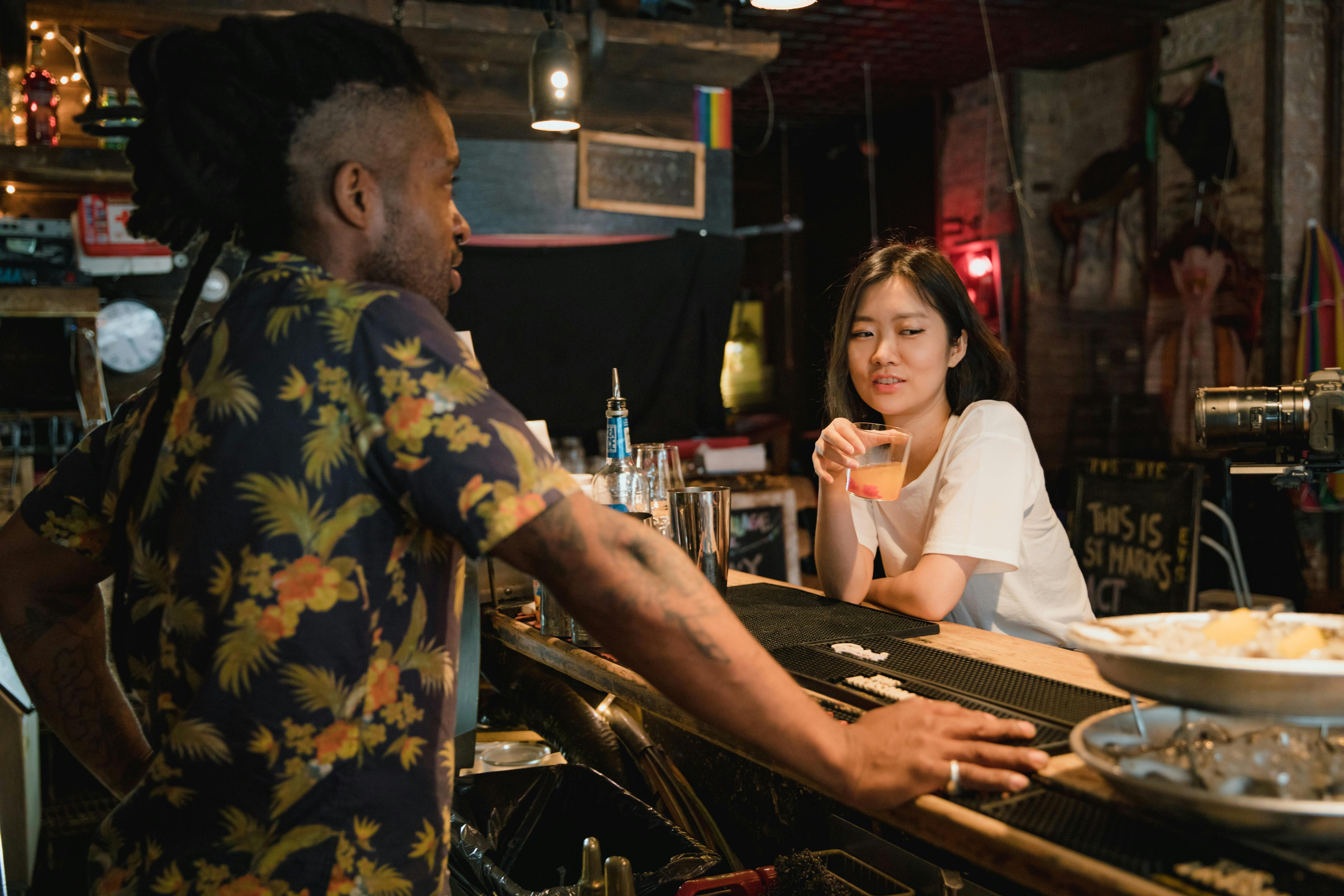 A bartender and customer engage in conversation at a stylish urban bar, highlighting leisure and diversity.