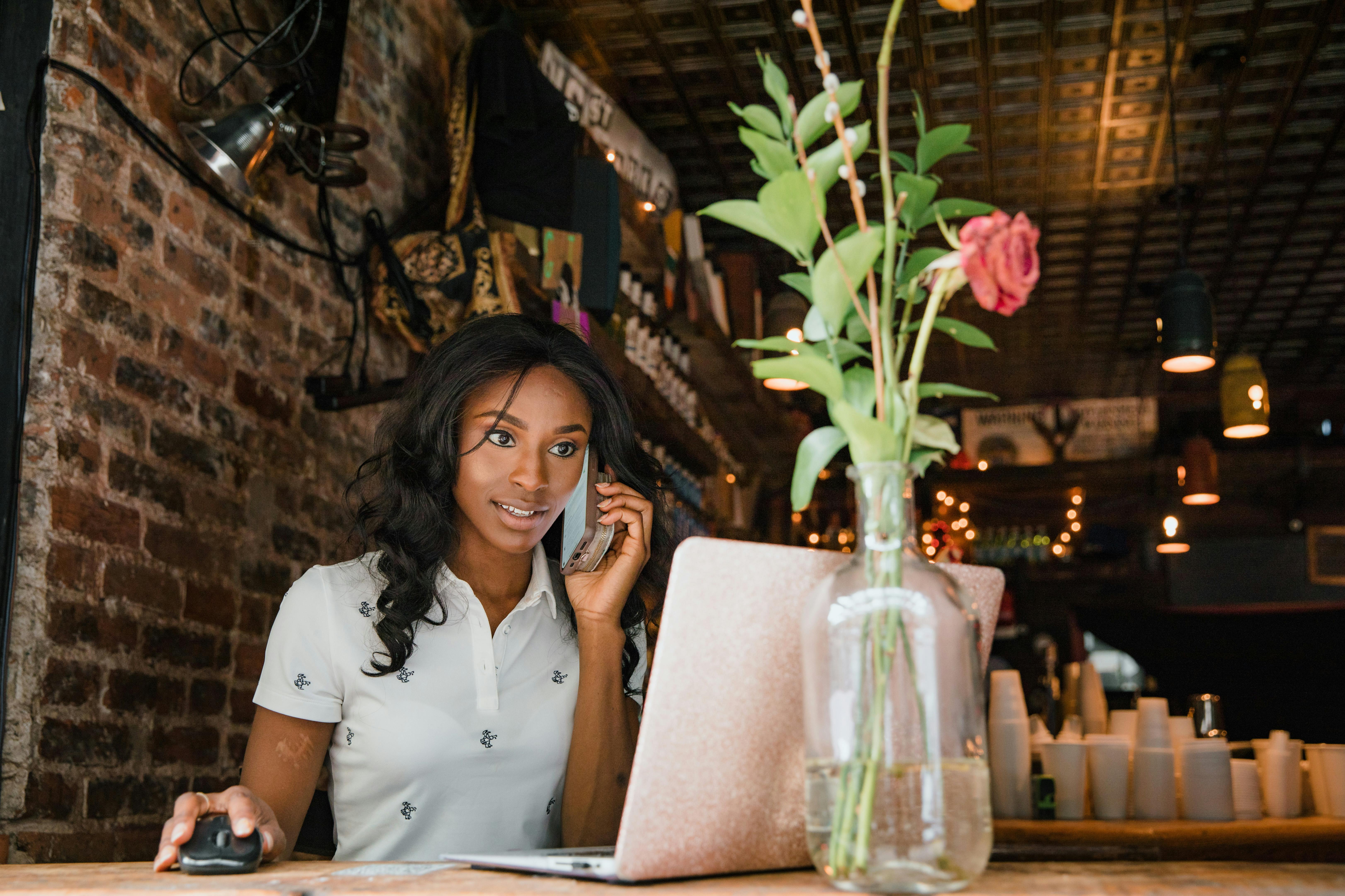 Woman working on laptop on a window sill while talking on the phone