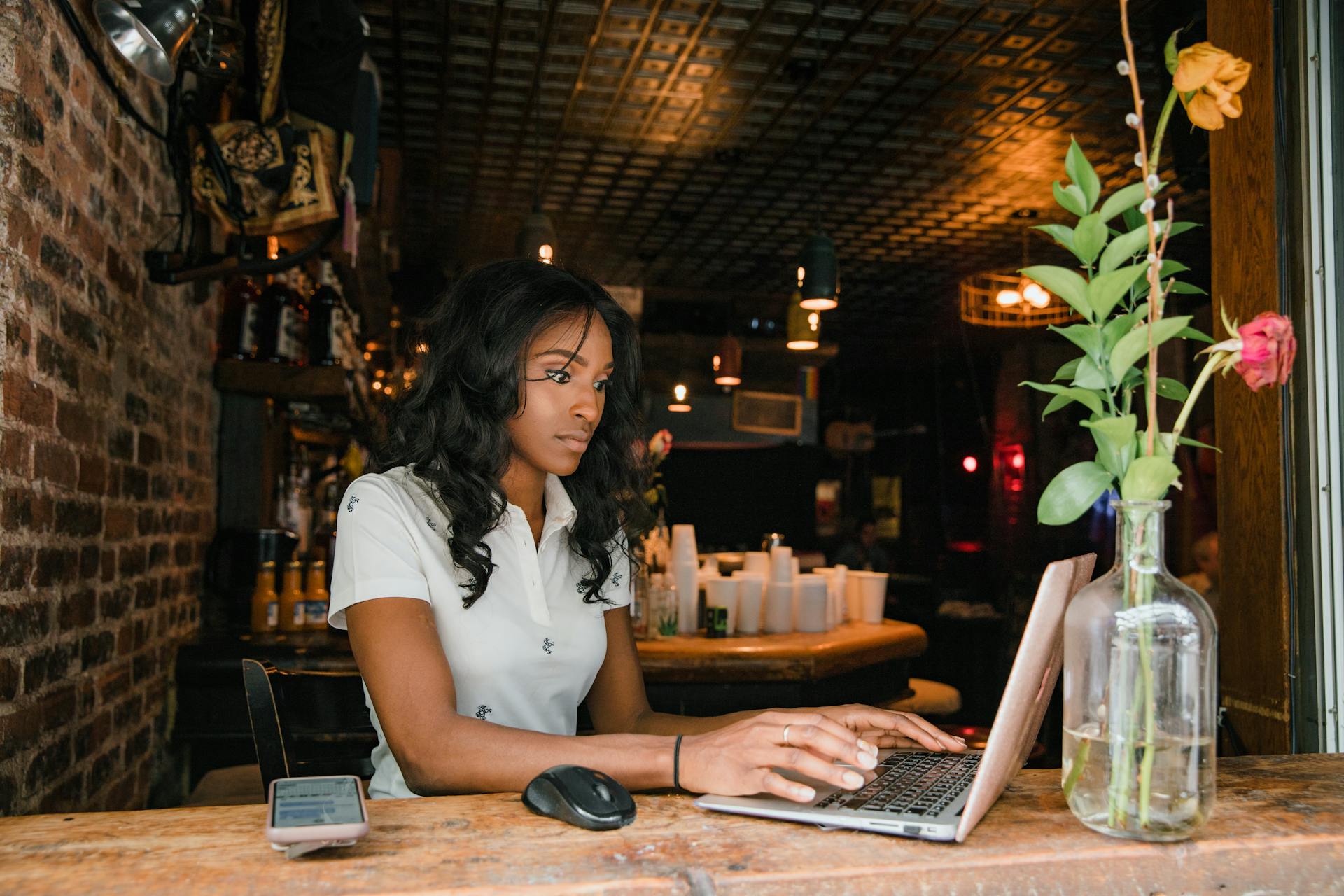 Young woman in a casual cafe working on her laptop, surrounded by rustic decor and flowers.