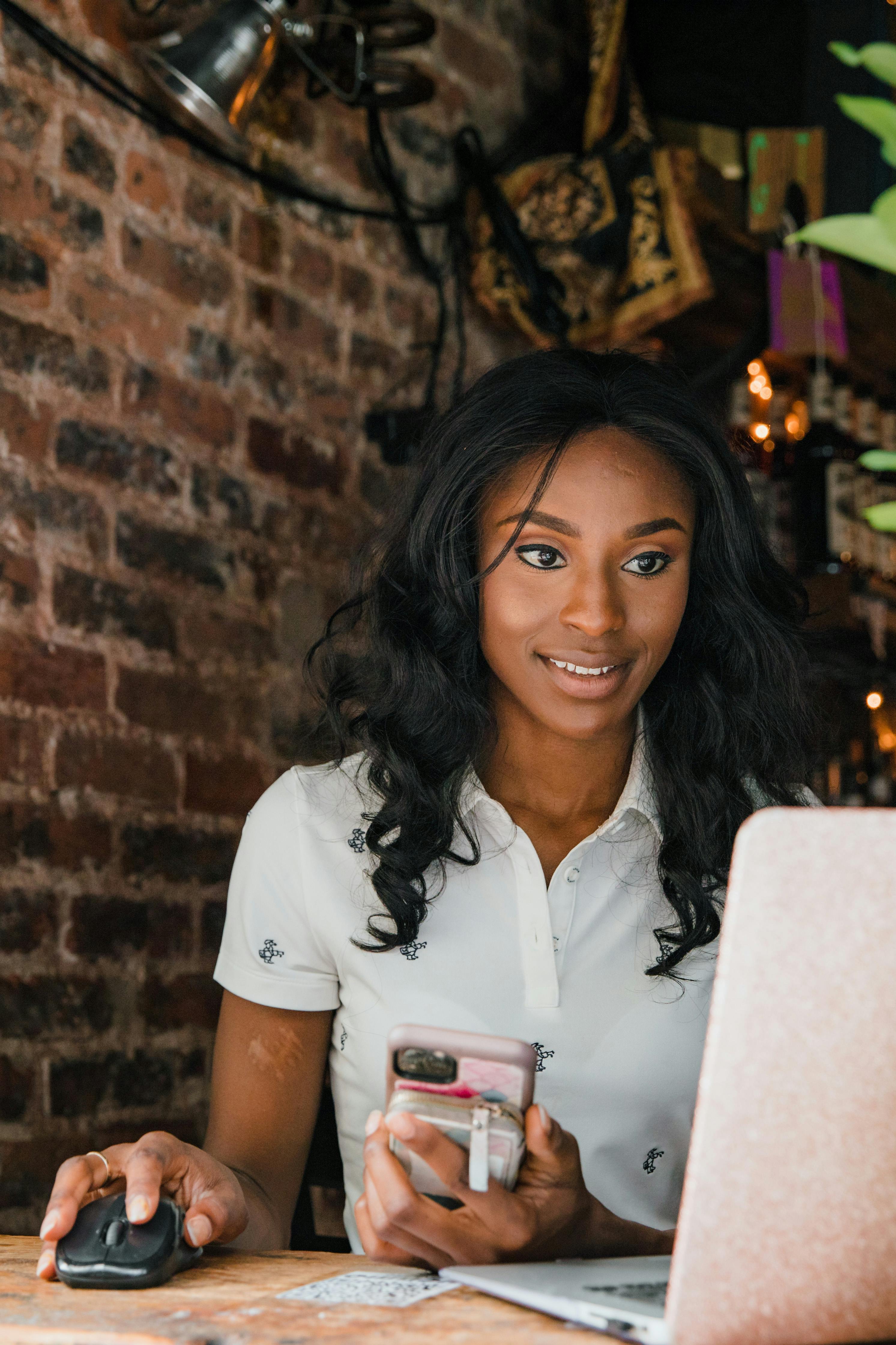 Professional woman using a laptop and smartphone at a cozy workplace with brick walls.