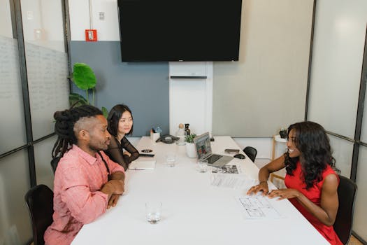 Three professionals engaged in a meeting around a white table in a modern office environment.