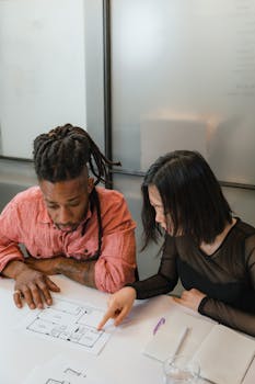 Two colleagues discussing floor plans during a business meeting in a modern office setting.