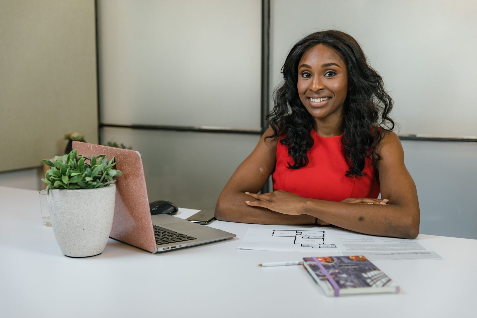 Professional woman in red sitting confidently at an office desk with a laptop and documents.