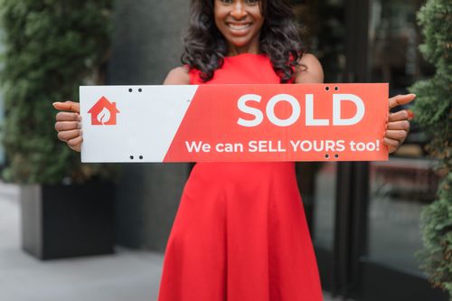 Free Smiling woman holding a 'Sold' sign, symbolizing successful real estate sales. Stock Photo