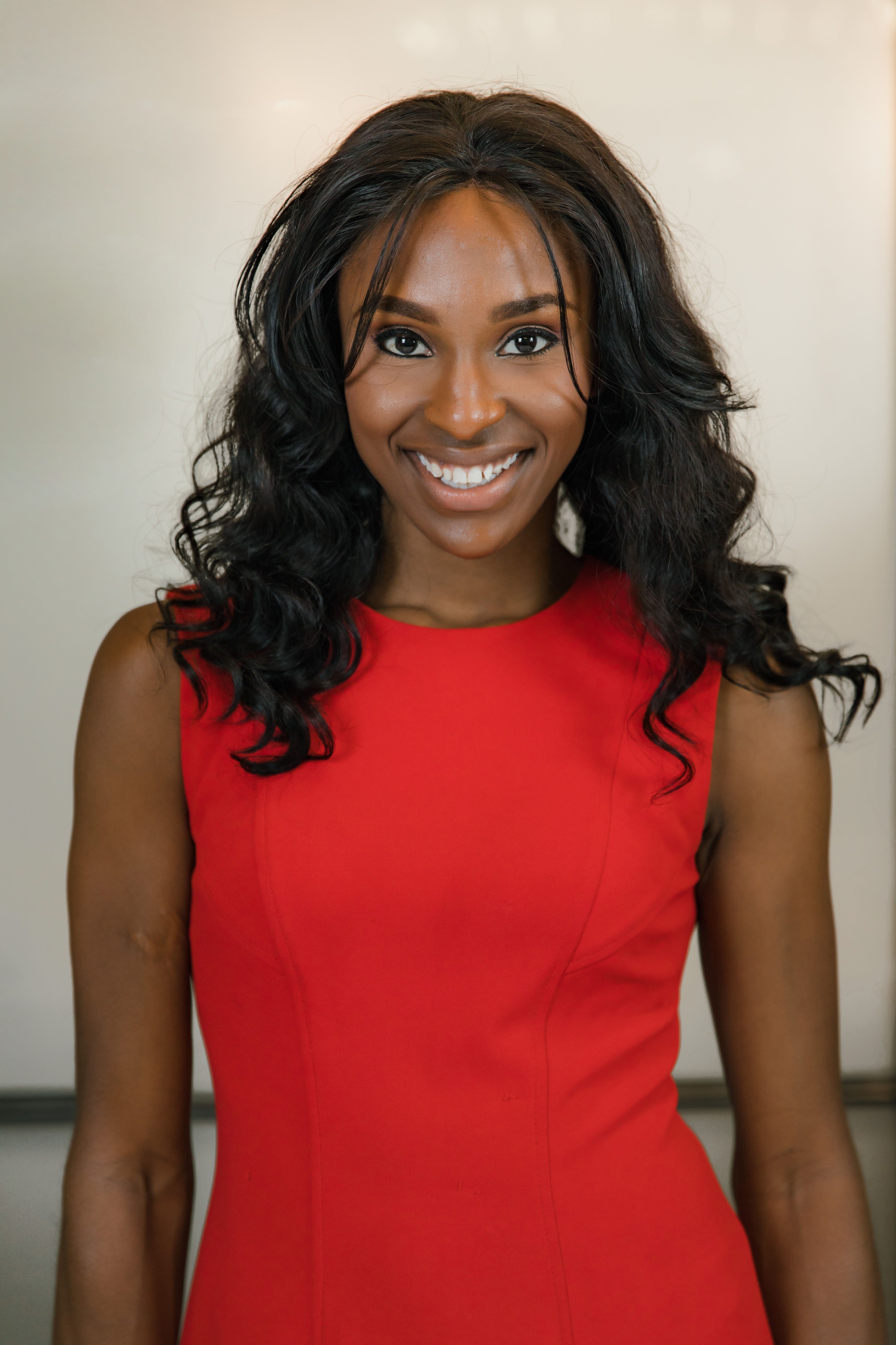 Confident woman smiling in a red dress, captured indoors with a warm, modern feel.