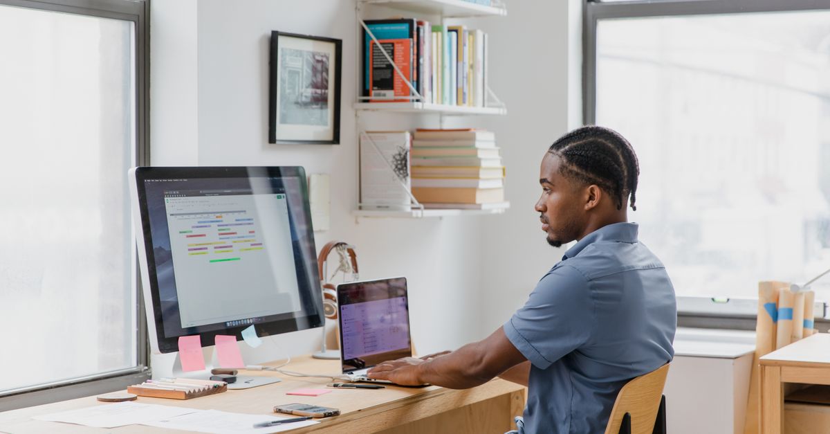 Pastor Prince D working on laptop in a modern office with bookshelf and church backdrop