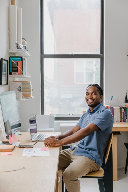 Free Smiling man working at desk in contemporary office space with window view. Stock Photo