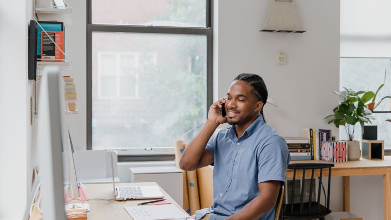Adult man engaged in office work, speaking on phone, showcasing a professional environment.
