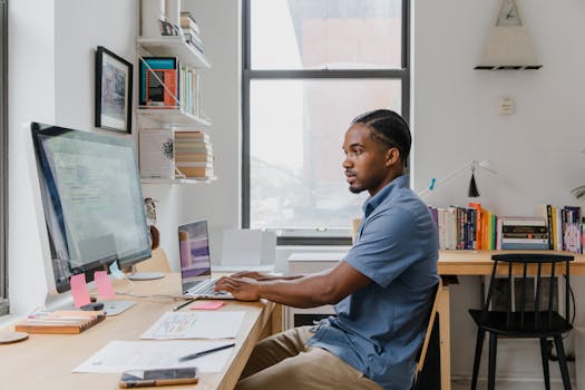 A professional man working on a laptop and computer in a stylish home office setting.