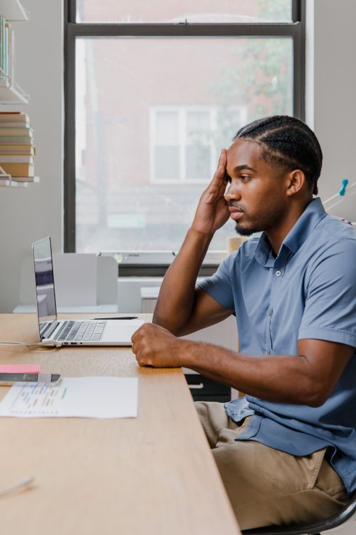 Free Man concentrating on laptop work at a home office desk with window view. Stock Photo