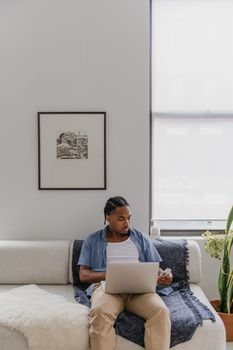 Casual young man using a laptop on a sofa in a modern living room.