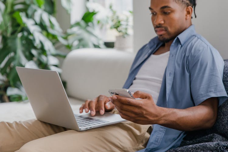 Man With Laptop On Lap Sitting On Sofa And Holding Phone