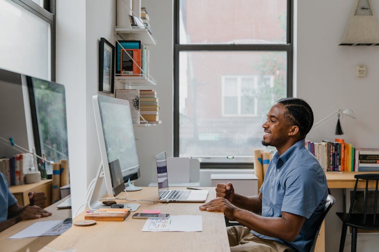 Man Sitting By Desk Using Computer And Laptop