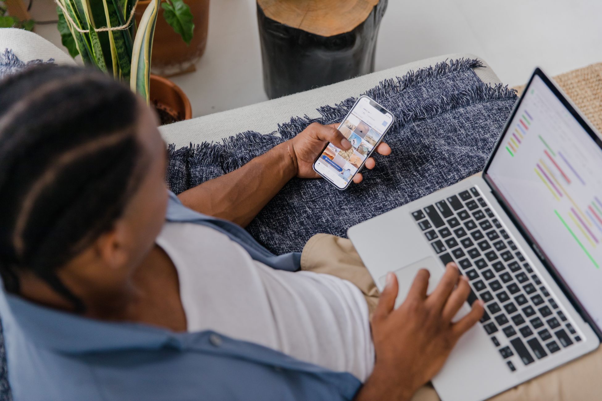 Man multitasking with a smartphone and laptop while sitting on a sofa indoors, top view.