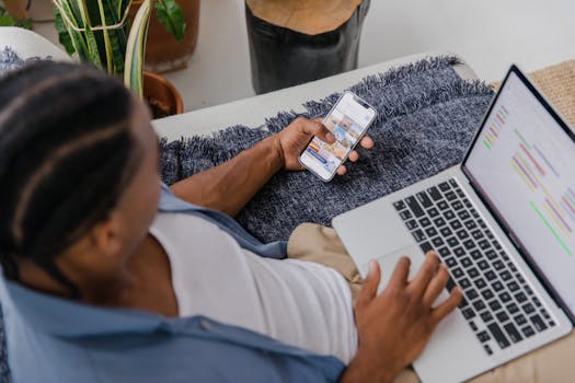 Man multitasking with a smartphone and laptop while sitting on a sofa indoors, top view.