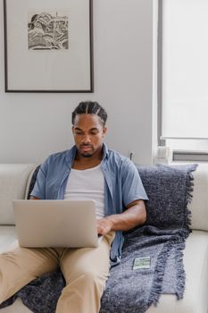 Adult man using laptop on sofa in modern living room. Casual and focused atmosphere.