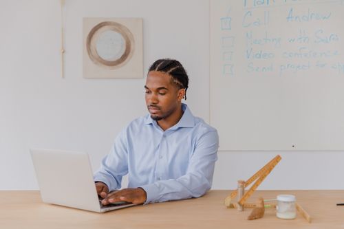 Free Businessman using laptop at desk with whiteboard notes in modern office environment. Stock Photo