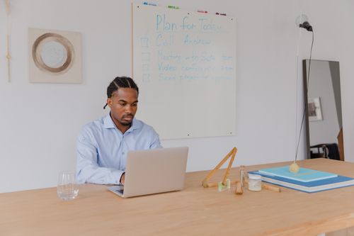 Free An adult man in a blue shirt working on a laptop in an office with a whiteboard. Stock Photo