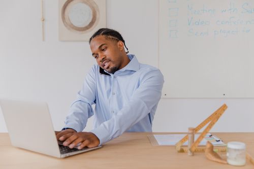 Free Businessman multitasking at desk with laptop and phone, showcasing productivity. Stock Photo