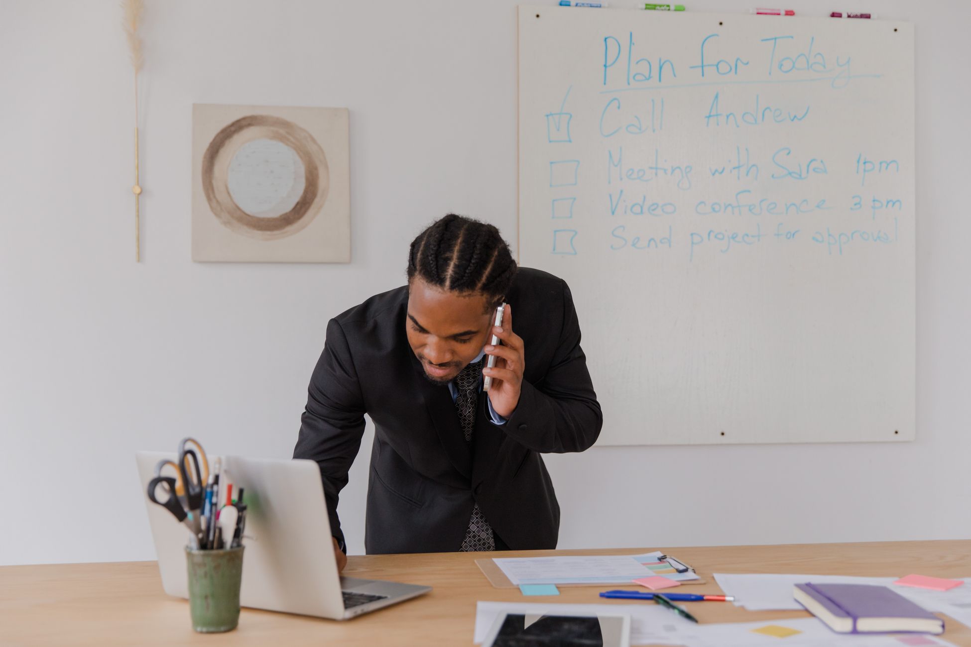 Businessman in an office making a call while working on a laptop with office supplies.